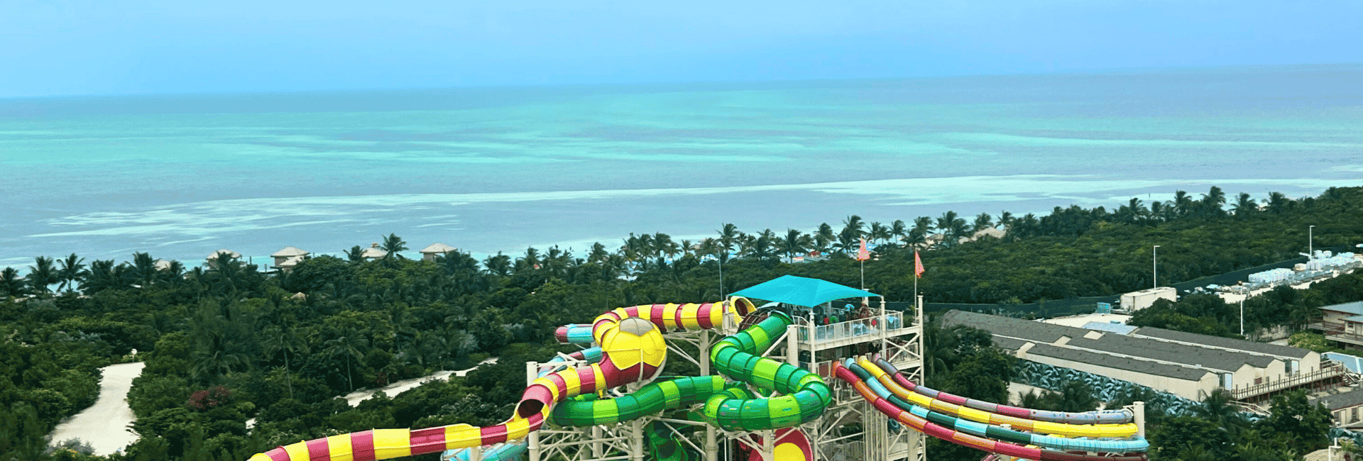 Bunte Wasserrutschen mit tropischen Bäumen auf Royal Caribbeans Privatinsel CocoCay mit einem türkisfarbenen Meer im Hintergrund.